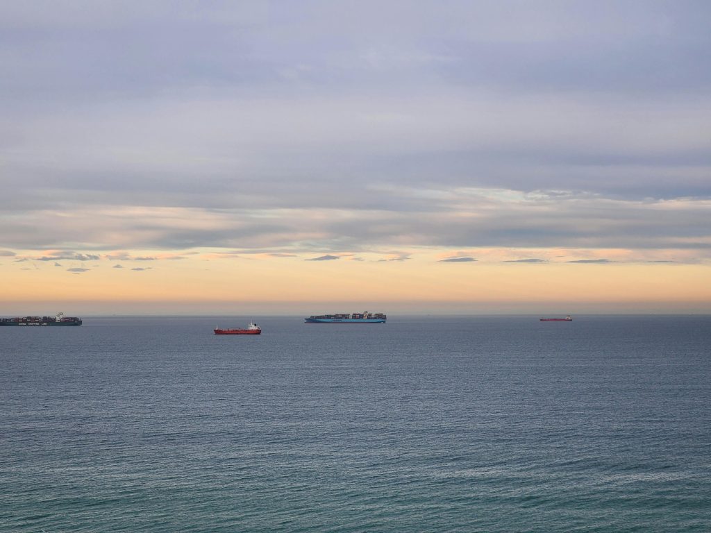 Serene ocean view with cargo ships under a colorful twilight sky.