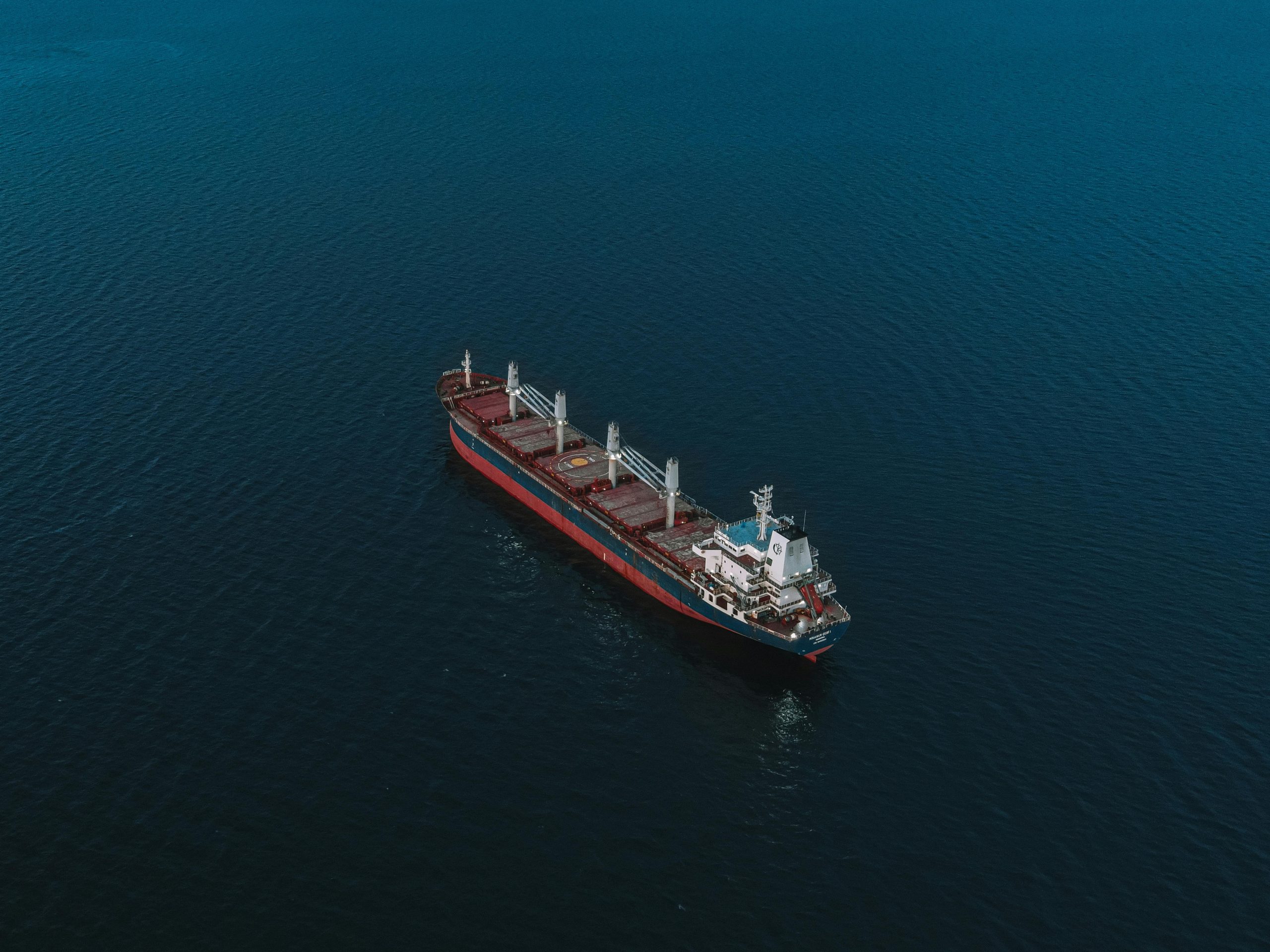 An aerial shot of a cargo ship navigating the open sea, surrounded by deep blue water.